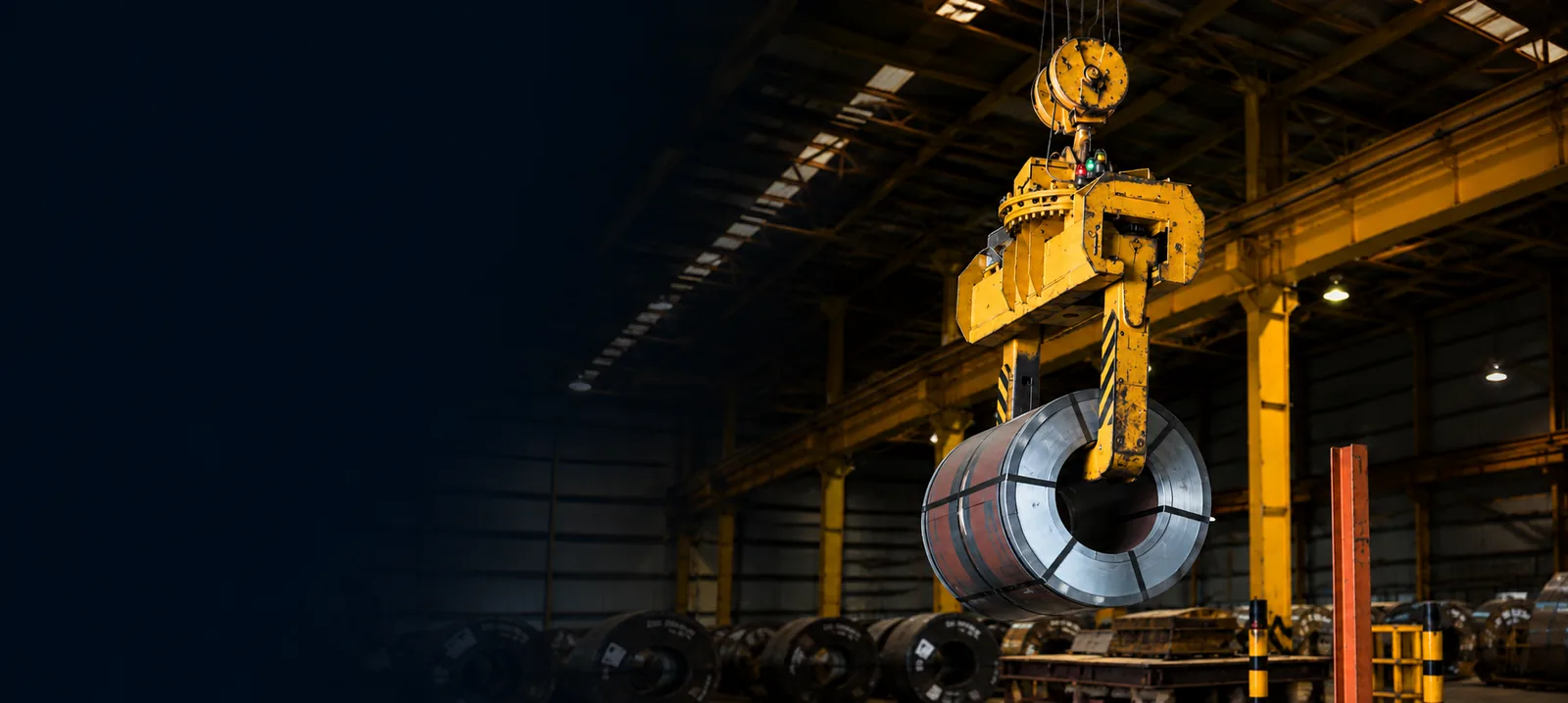 Dark workshop, a yellow hook block lifting a large steel coil